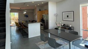 A modern kitchen with a central island, dining area with chairs, and a staircase leading to an upper level. - Modern Townhouse in Palm Springs (Palm Springs)
