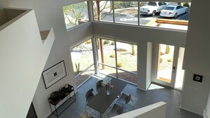 A multi-level interior with a dining area, staircase, and large windows offering a view of parked cars and desert landscape. - Modern Townhouse in Palm Springs (Palm Springs)