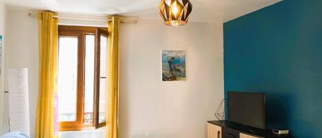 Un espacio habitable pequeño con cama, una mesita, televisor y radiador.