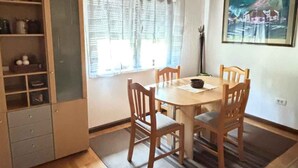 A dining area with a wooden table and chairs, a window with curtains, and a painting on the wall.