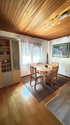 A dining area with a wooden table and chairs, a window with curtains, and a painting on the wall.