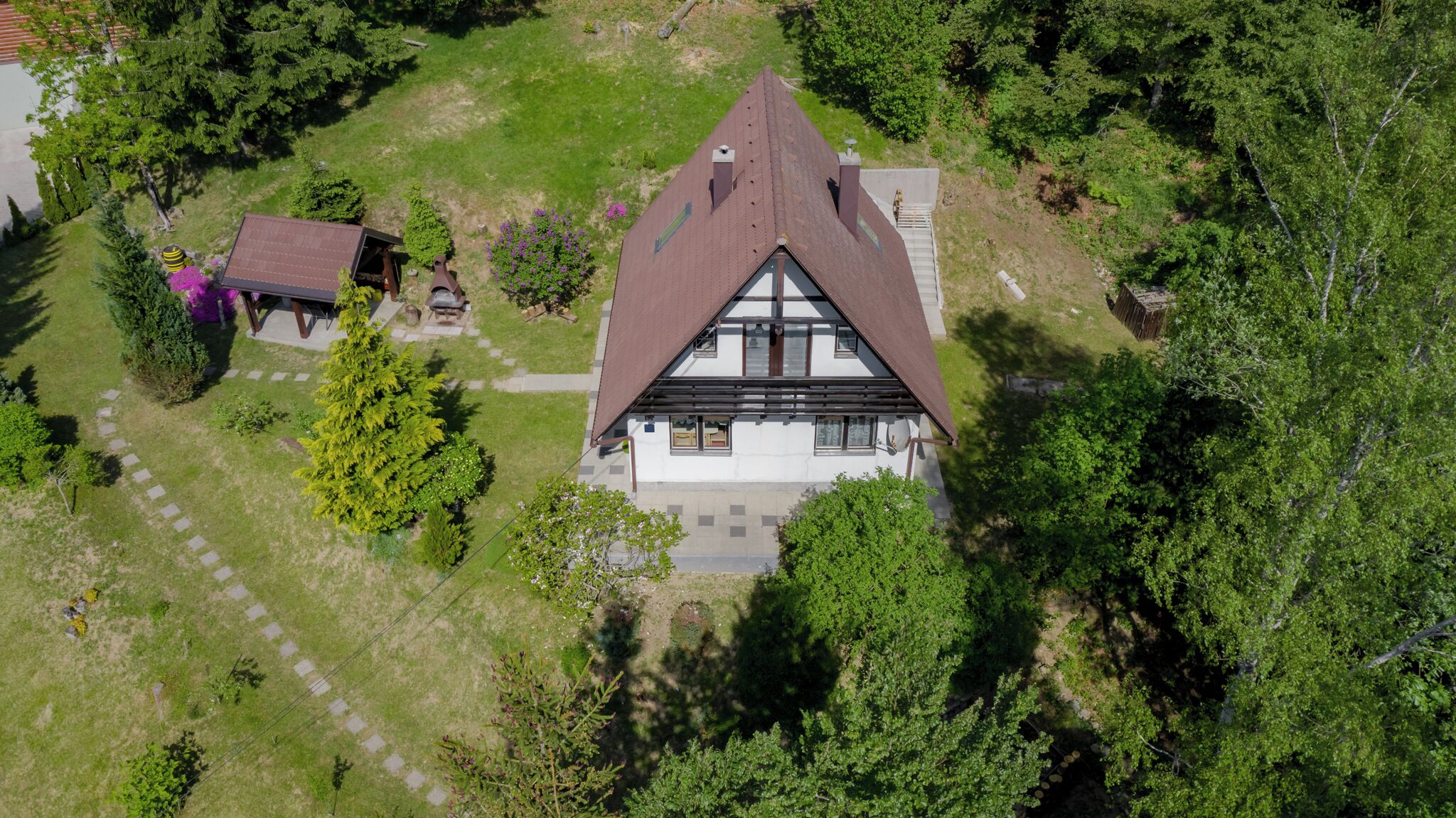 A two-story house with a steeply pitched roof, surrounded by a well-maintained lawn and trees.