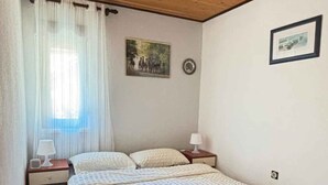 A bedroom with a wooden ceiling, a bed with a white bedspread, a nightstand with a lamp, and a window with curtains.