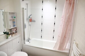 Et badeværelse med bruseniche, toilet, vask og spejl.