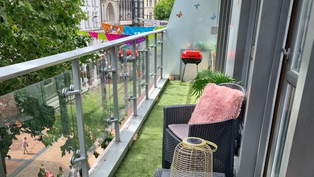 Un balcon avec un revêtement de sol en gazon synthétique, des meubles en osier et une rambarde en verre.
