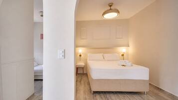 A hotel room with a bed, bedside lamps, a ceiling fan, and a view through an archway to another room.
