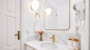 A bathroom with a white marble sink, gold fixtures, a hairdryer, and a vase with flowers.