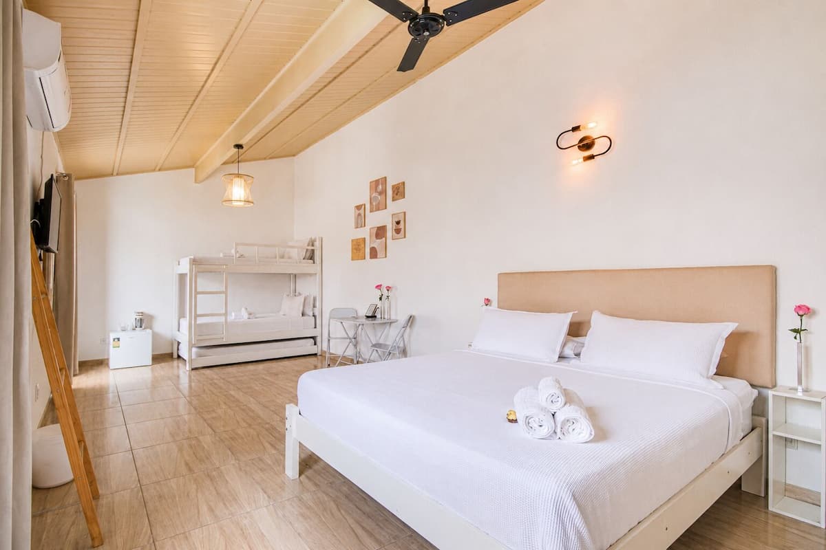 Une chambre avec un lit superposé, un bureau, une chaise, un lit avec des serviettes pliées et un ventilateur de plafond.