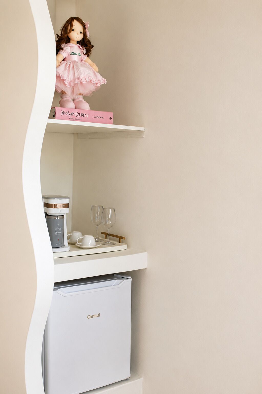 Una muñeca en un estante, una cafetera y un refrigerador.