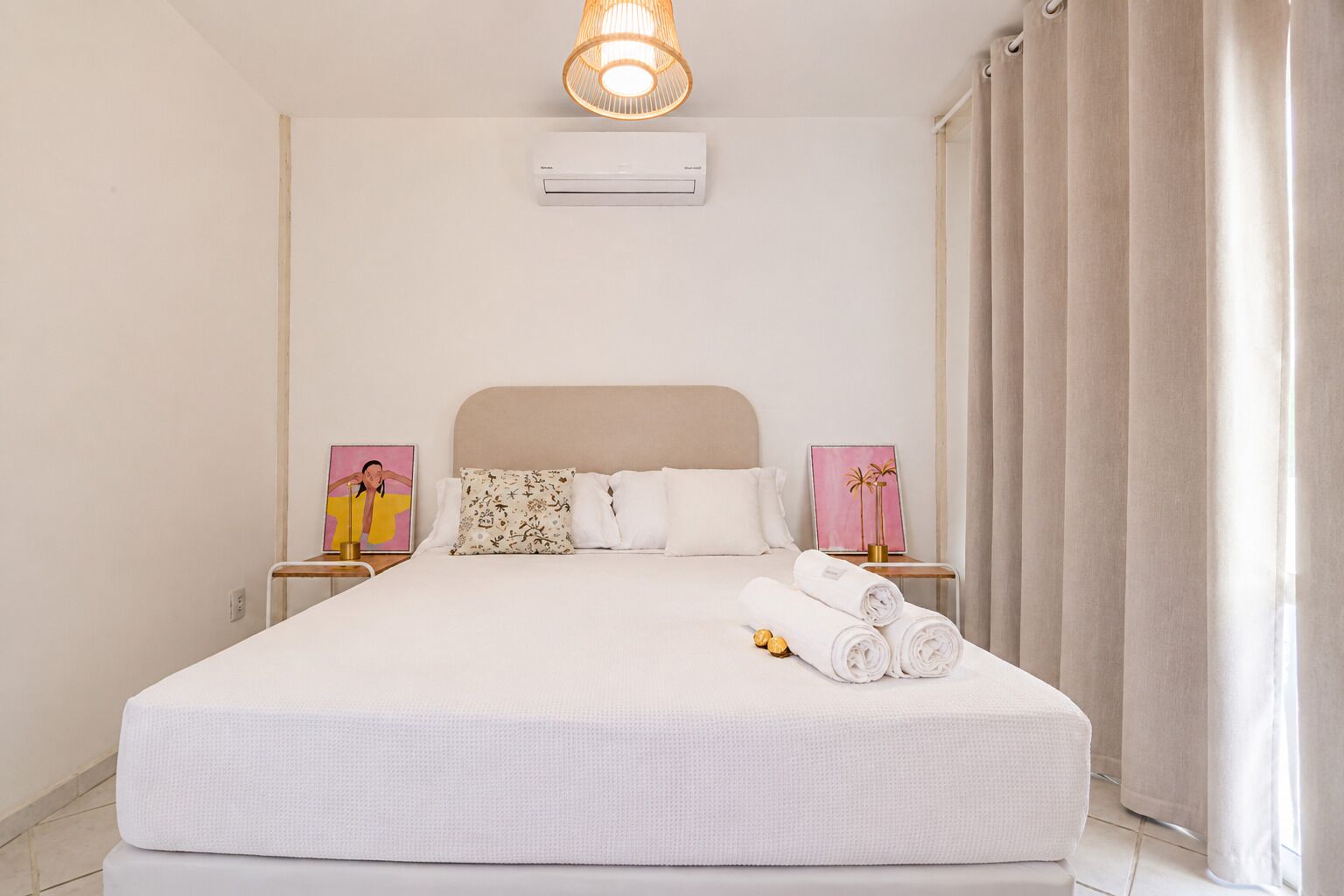 A neatly made bed with white linens, a headboard, and two bedside tables with lamps and framed pictures.