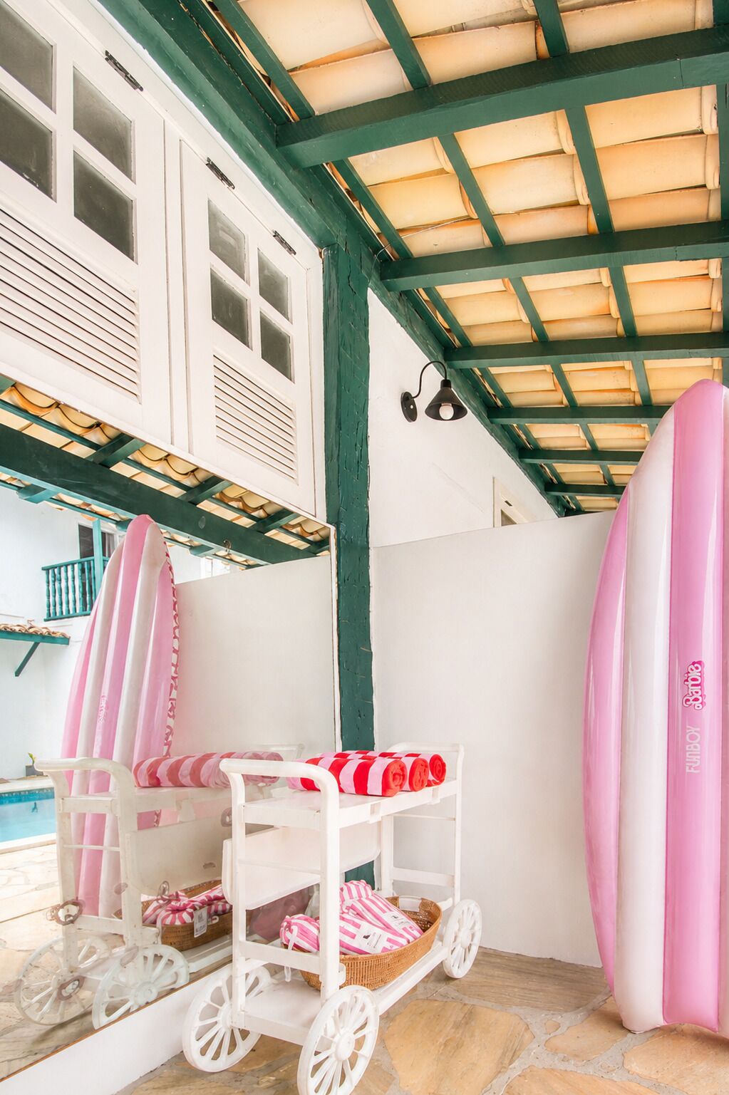 Quarto com piscina, carrinho com toalhas rosa e brancas e uma prancha de surf.