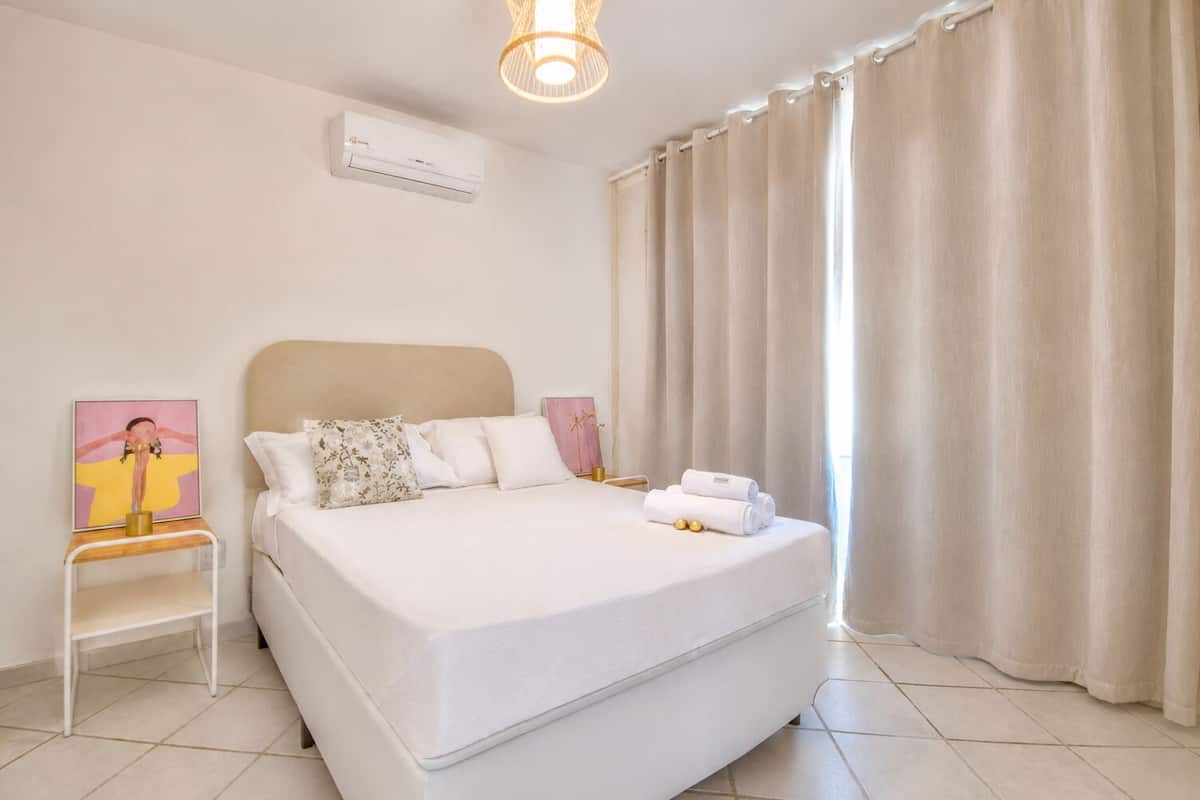 Une chambre à coucher comprenant un lit, une table de chevet, un appareil de climatisation et une fenêtre avec des rideaux.