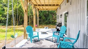 A covered porch with turquoise Adirondack chairs, a grill, and a swing set.