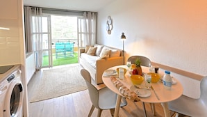 Un salón acogedor con un sofá, una mesa de comedor con una botella de Nespresso y vistas a un área exterior verde a través de la ventana.
