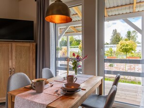 Un comedor con una mesa de madera, sillas, un florero con flores y un televisor en la pared.