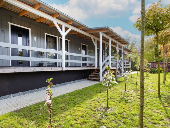 Un edificio moderno con un área exterior techada, un sendero pavimentado y un jardín con árboles jóvenes.