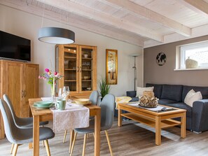 Un salon moderne comprenant un coin repas, des meubles en bois, un téléviseur et un grand meuble de rangement.