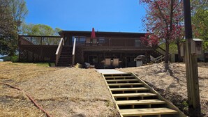 Ein zweistöckiges Holzhaus mit einer überdachten Veranda, einer Holztreppe, die zum oberen Stockwerk führt, und einer kleinen Außenbereich-Sitzgelegenheit.