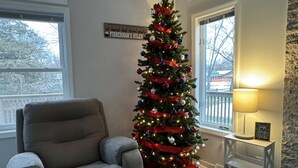 Ein Wohnzimmer mit einem grauen Sessel, einem Weihnachtsbaum, einer Lampe und einem Kamin.