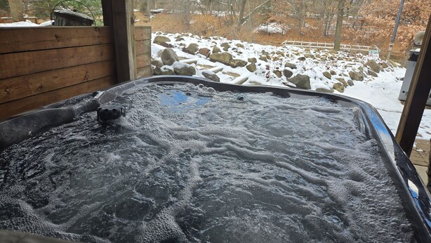 Ein Whirlpool mit einer Holzterrasse und Blick auf eine verschneite Landschaft mit Felsen und Bäumen.