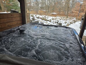 Un bain à remous doté d’une terrasse en bois et offrant une vue sur un paysage enneigé, avec des rochers et des arbres.