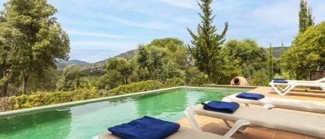 A poolside area with lounge chairs and a view of the surrounding greenery and hills.