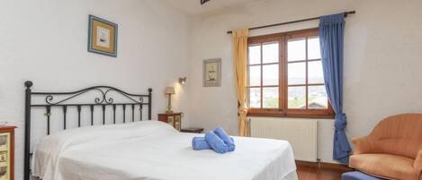 Ein Schlafzimmer mit Bett, Sessel, einem Fenster mit Vorhängen und einer Pendelleuchte.