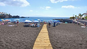 Ein Sandstrand mit einer Holzpromenade, die zum Wasser führt, Sonnenschirmen und Liegestühlen.