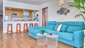 Ein modernes Wohnzimmer mit einem blauen Sofa, Holzschemeln und einer Küche im Hintergrund.