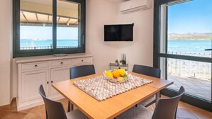 A dining area with a table set for two, a large window with a view of the sea, and a flat-screen TV mounted on the wall. - Donatella by Interhome (Cannigione)