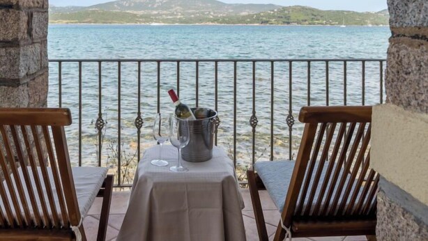 A balcony with a table set for two, overlooking a body of water with hills in the distance. - Donatella by Interhome (Cannigione)