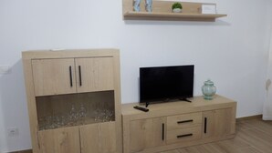 Un meuble en bois sur lequel est posée une télévision, avec une télécommande et un bocal en verre.