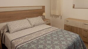 Une chambre à coucher avec une tête de lit en bois, un lit avec une literie à motifs, une table de chevet avec une lampe, un miroir et une commode en bois.