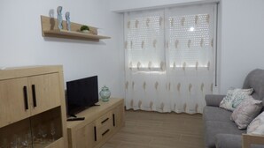 Un salon avec un téléviseur posé sur un meuble en bois, un vase en verre et un canapé gris agrémenté de coussins à motifs.
