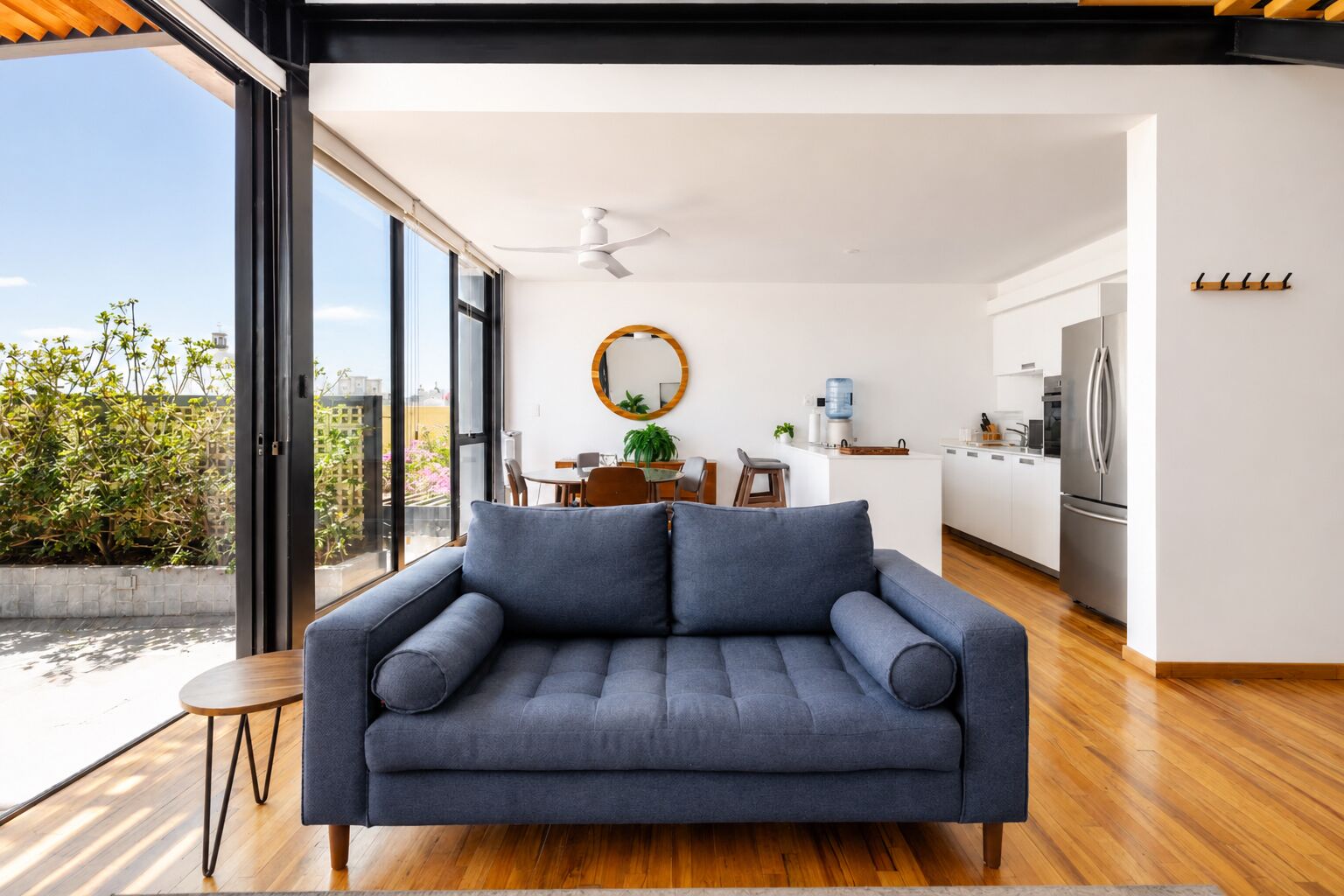 A modern living room with a sofa, a dining area, and a kitchen.