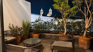 An outdoor patio with wicker furniture, potted plants, and a view of a cathedral at night. - Cathedral Fantastic View Loft (Heroica Puebla de Zaragoza)