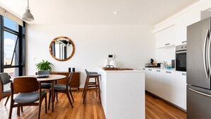 A modern kitchen with wooden flooring, white cabinetry, a stainless steel refrigerator, and a dining area with a round mirror. - Cathedral Fantastic View Loft (Heroica Puebla de Zaragoza)