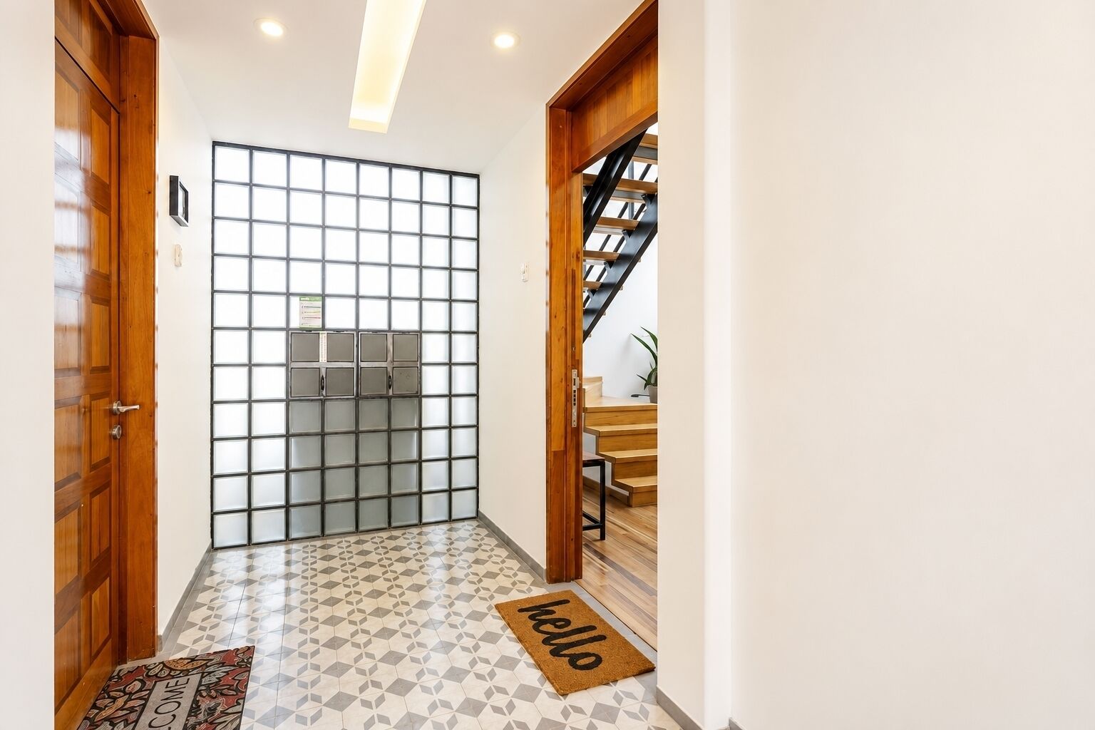 A hallway with a wooden door, a frosted glass partition, a patterned floor, and a 'hello' mat.