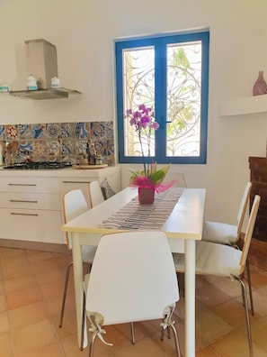 Un comedor con una mesa blanca, sillas y un jarrón decorativo con flores.
