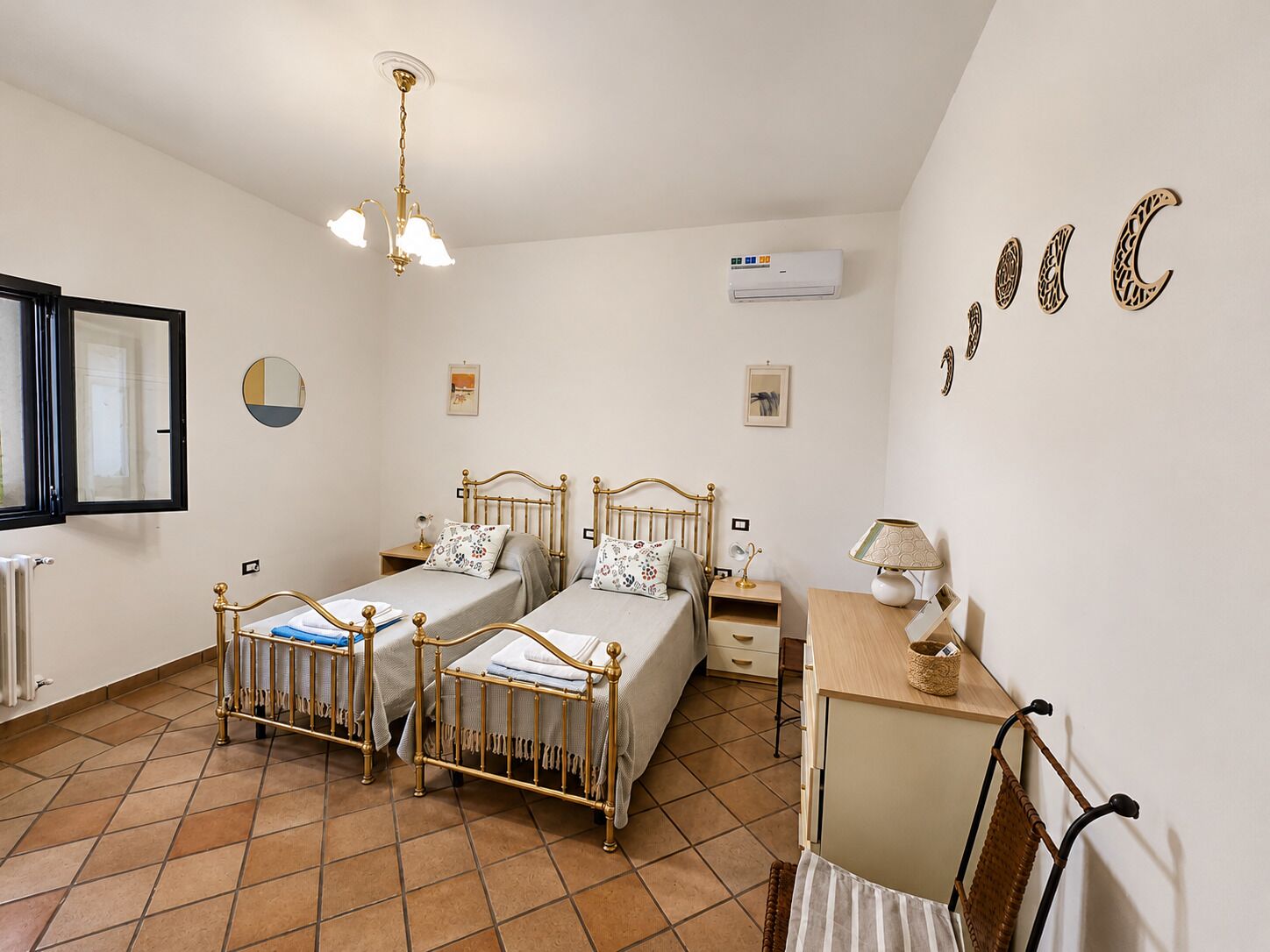 A bedroom with two beds, a desk, a chair, a radiator, an air conditioner, and a window.