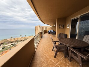 A balcony with a view of the sea, a table and chairs, and a door leading to an interior space.