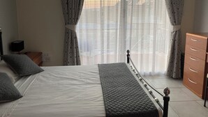Une chambre à coucher avec un lit, une commode, une table de chevet et une fenêtre avec des rideaux.