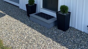 Un bâtiment blanc avec une porte noire, un drapeau et deux plantes en pot.
