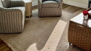 Une pièce dotée de grandes fenêtres donnant sur un plan d’eau, comprenant deux fauteuils à motifs, une petite table ronde et une table d’appoint en osier.