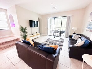 Relax in this stylish living room with a large flat-screen TV, comfortable sofa, and armchair, leading to a patio with dining area.