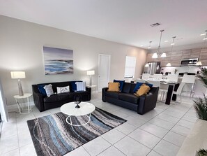 Relax in this stylish living room with a sofa, coffee table, and abstract art, offering a view of the adjacent kitchen and dining area.