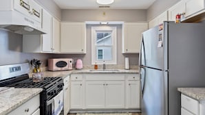 Una cocina con gabinetes blancos, un refrigerador de acero inoxidable, una estufa a gas y un microondas.