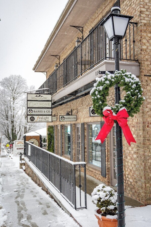 A brick building with a balcony, a red bow on a post, and a snow-covered ground.