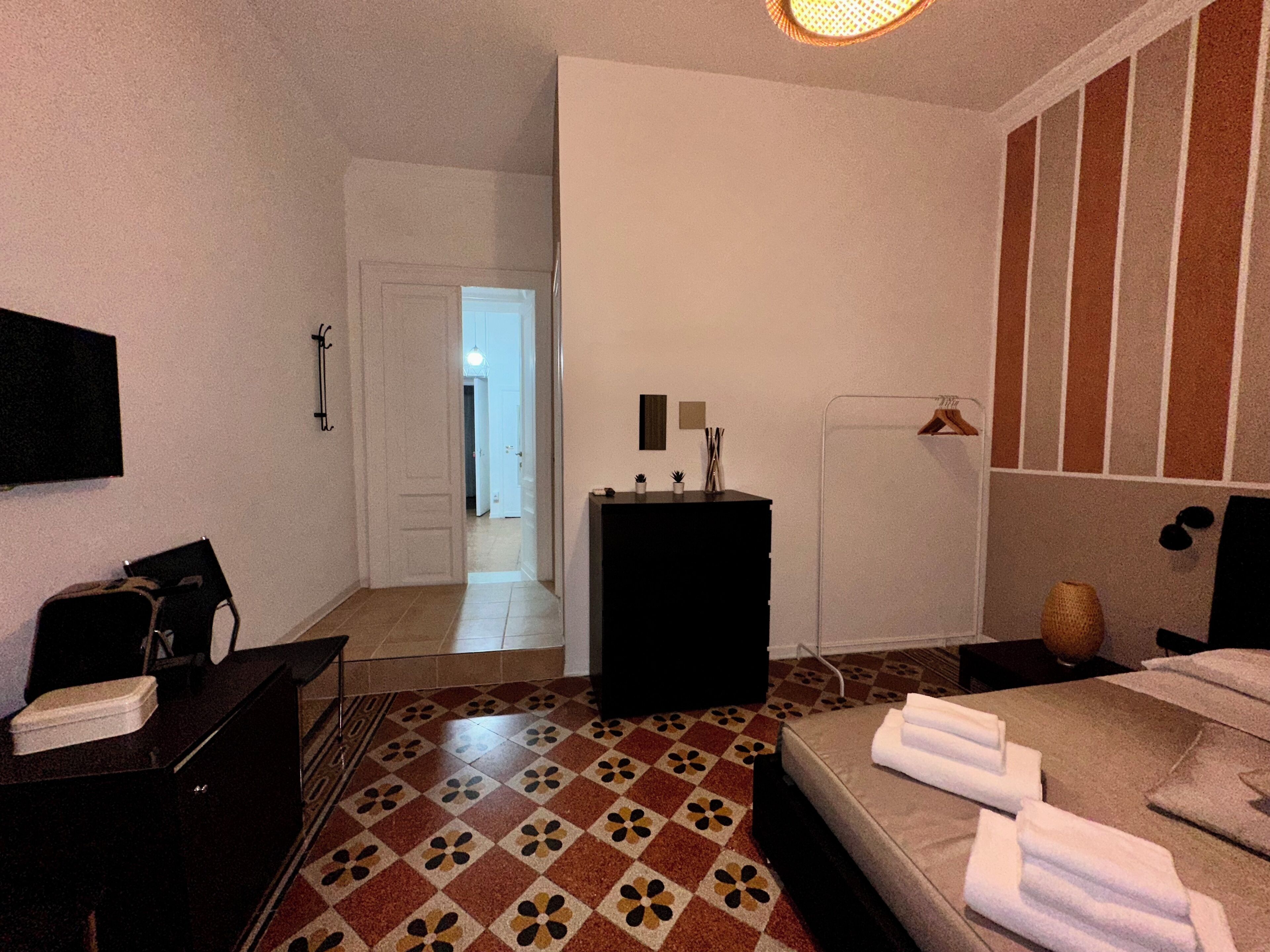 Ein Hotelzimmer mit Bett, Schreibtisch, Stuhl, Fernseher, einem kleinen Tisch mit Pflanzen und einer Tür zu einem weiteren Raum.