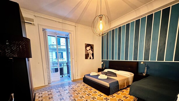 A hotel room with a bed, a nightstand, a lamp, a picture on the wall, and a patterned floor. - Mammina Home Napoli - Santa Lucia (Naples)